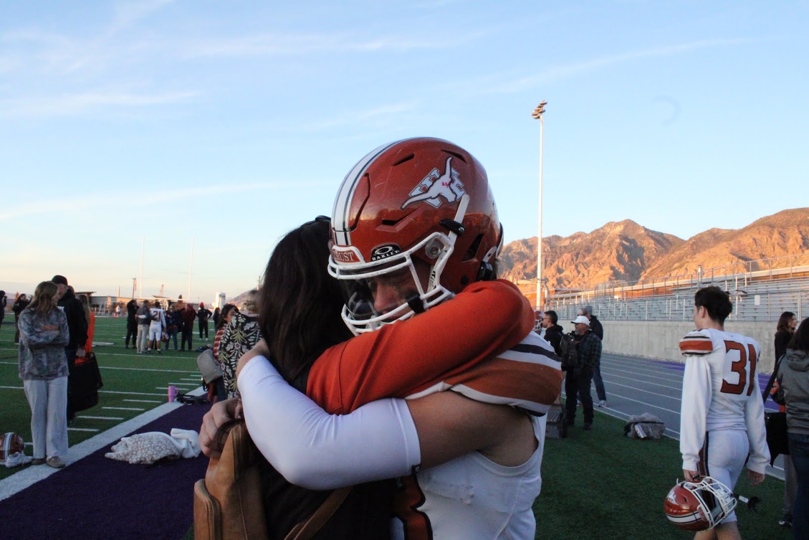 Football player in red helmet embracing a family member after the game