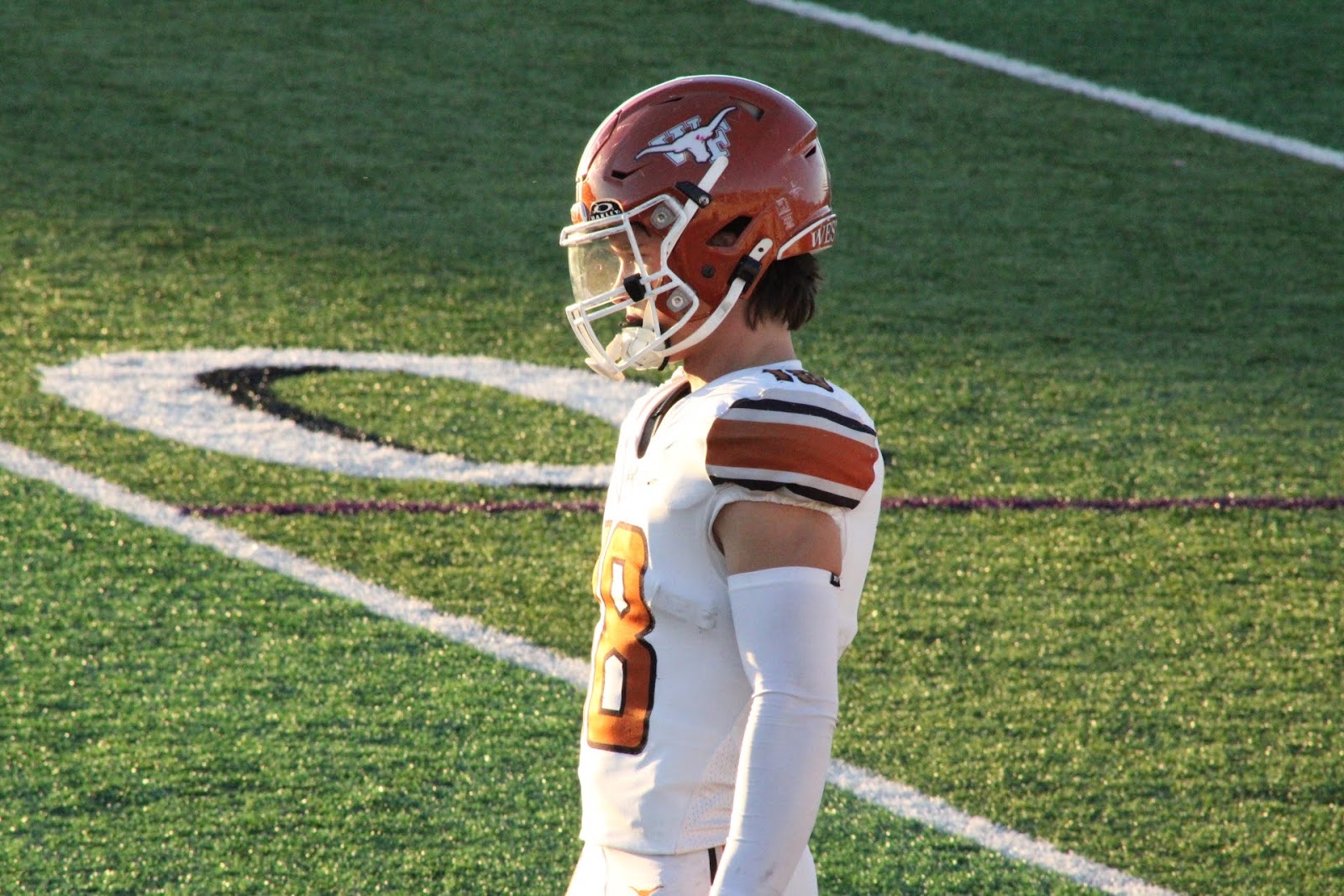 Football player in white and orange uniform standing alone on the field at night