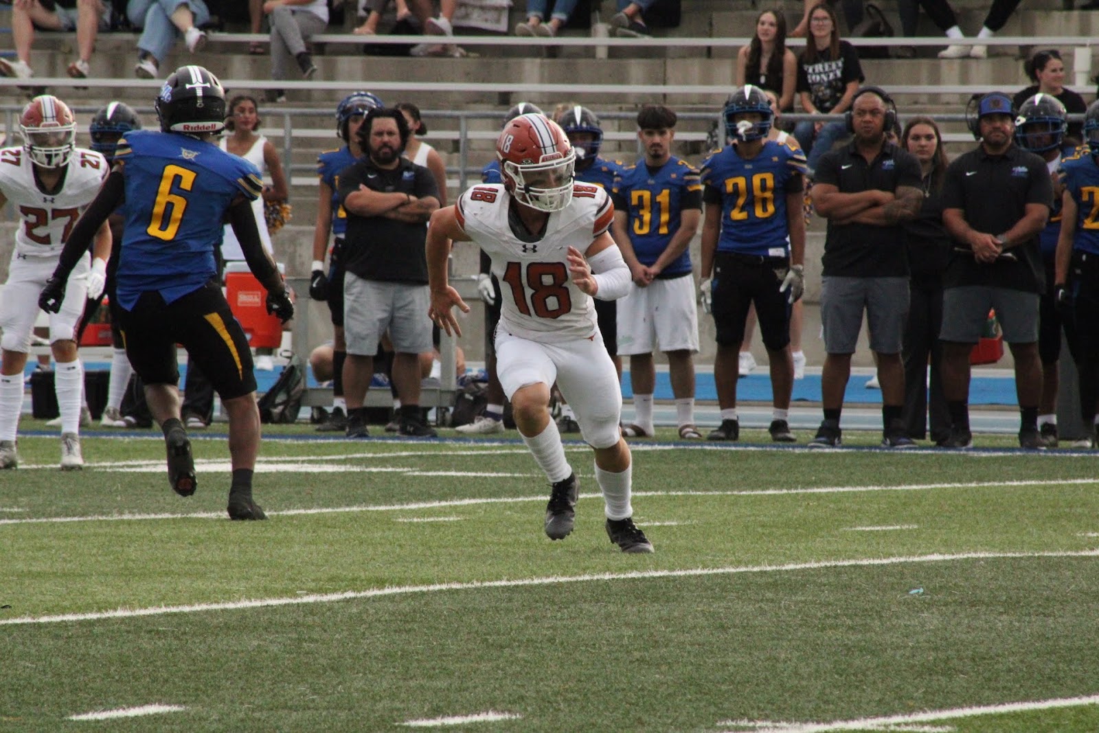 Football player number 18 sprinting past the team bench with the ball